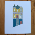 Illustration of a two-story house with yellow and blue exterior on a light blue background, placed on a wooden surface.